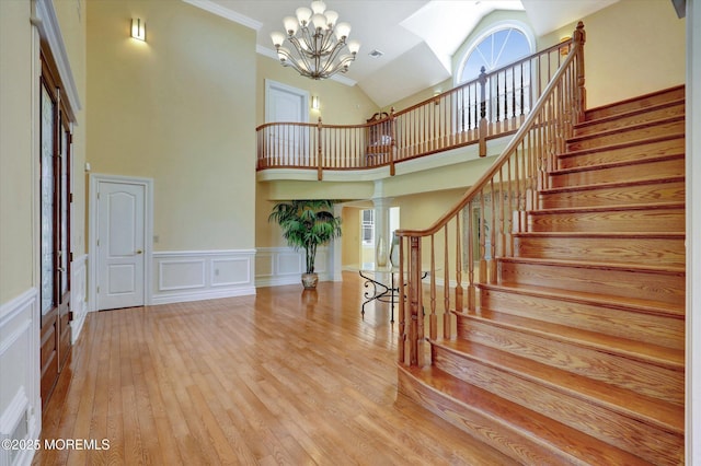 stairs with hardwood / wood-style floors, a decorative wall, wainscoting, high vaulted ceiling, and a notable chandelier