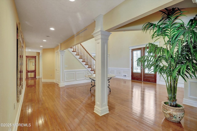 entrance foyer with light wood-type flooring, a decorative wall, stairs, and wainscoting
