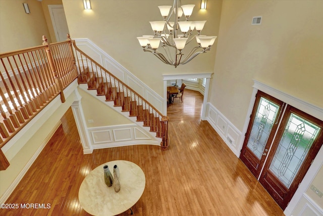 entryway with a decorative wall, wood finished floors, an inviting chandelier, a high ceiling, and visible vents
