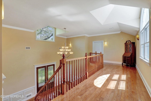 corridor featuring a wealth of natural light, a notable chandelier, wood finished floors, and an upstairs landing
