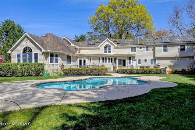 back of house with an outdoor pool, a yard, a patio area, and solar panels