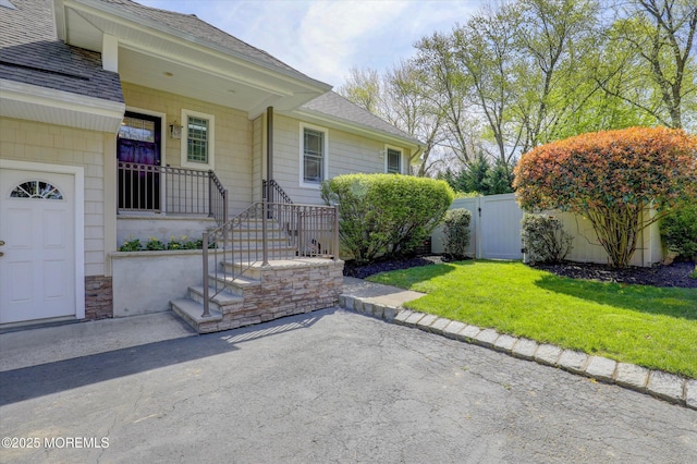property entrance with roof with shingles, a gate, fence, a patio area, and a yard