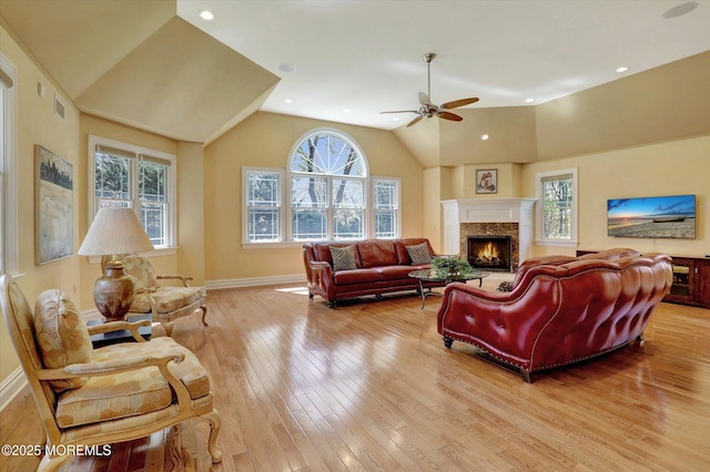 living area with hardwood / wood-style flooring, lofted ceiling, a ceiling fan, and a warm lit fireplace