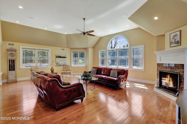 living room featuring light wood-type flooring, a premium fireplace, baseboards, and ceiling fan