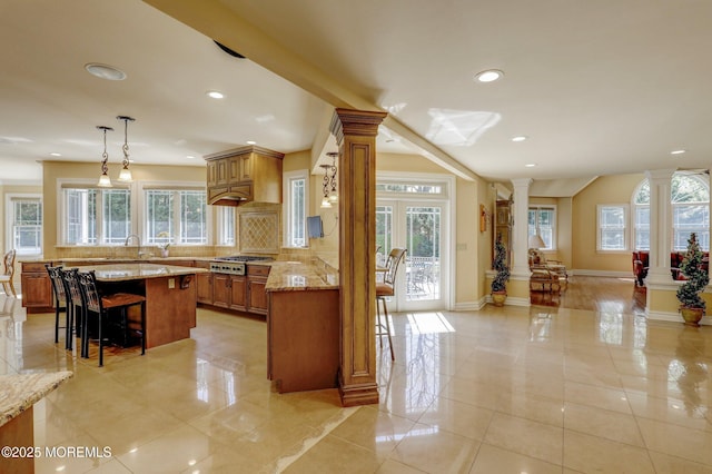 kitchen featuring a breakfast bar, brown cabinetry, recessed lighting, and decorative columns