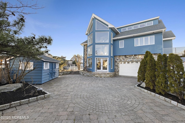exterior space featuring curved driveway, roof with shingles, french doors, stone siding, and a garage