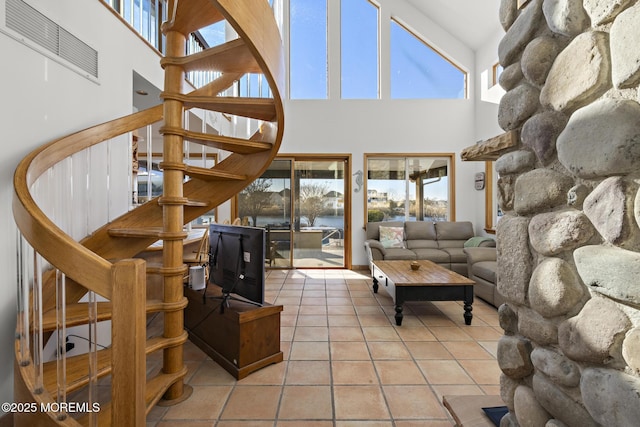 living area with plenty of natural light, stairs, tile patterned flooring, and a towering ceiling