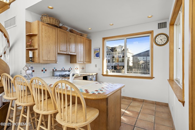 kitchen with visible vents, light countertops, decorative backsplash, and a kitchen breakfast bar