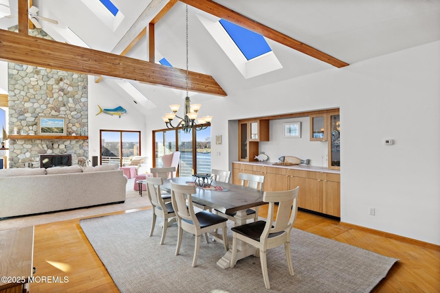 dining area featuring light wood-type flooring, baseboards, beam ceiling, a skylight, and a stone fireplace