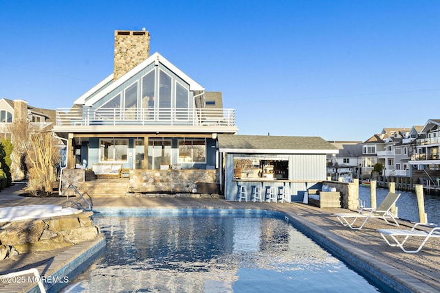 back of property featuring a balcony, a chimney, outdoor dry bar, and a patio area