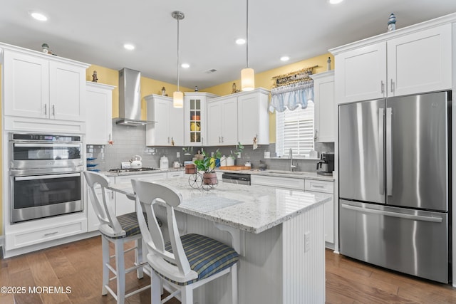 kitchen with stainless steel appliances, white cabinets, a sink, and wall chimney range hood