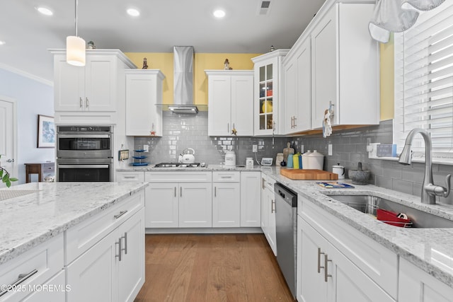 kitchen featuring wall chimney range hood, white cabinets, visible vents, stainless steel appliances, and a sink