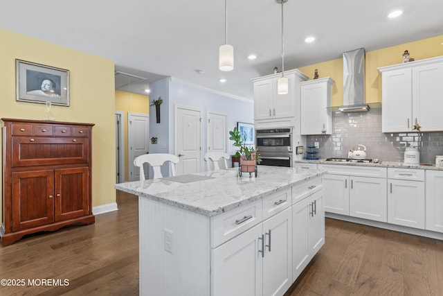 kitchen featuring wall chimney range hood, appliances with stainless steel finishes, a kitchen island, and dark wood finished floors