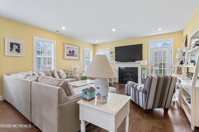 living room featuring a glass covered fireplace, recessed lighting, and dark wood-type flooring