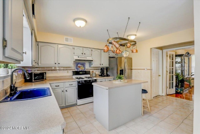 kitchen with visible vents, range with gas stovetop, under cabinet range hood, a sink, and stainless steel fridge with ice dispenser