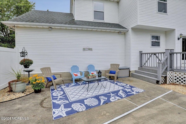 back of house featuring a wooden deck, roof with shingles, and a patio