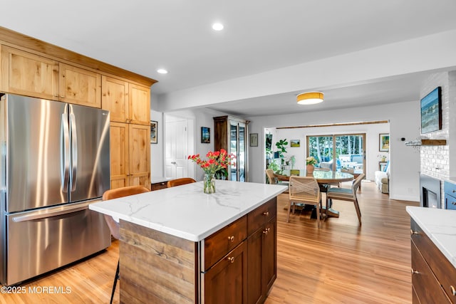 kitchen featuring freestanding refrigerator, light wood-style flooring, a center island, recessed lighting, and light stone counters
