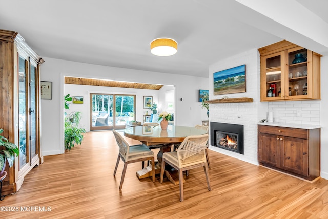 dining area featuring light wood finished floors, a brick fireplace, and baseboards