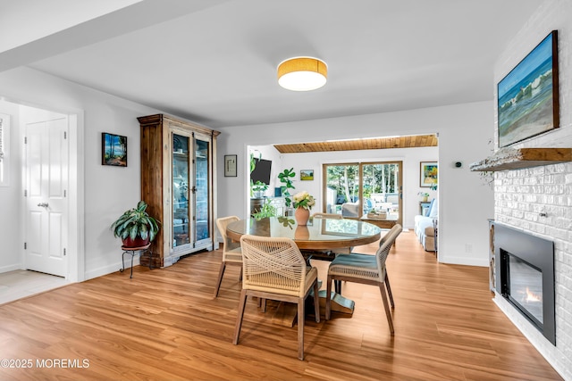 dining area featuring a brick fireplace, light wood-type flooring, and baseboards