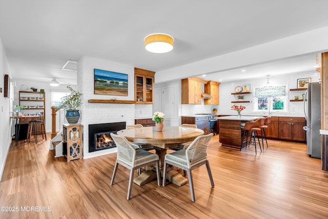 dining space with a brick fireplace, light wood finished floors, and a ceiling fan