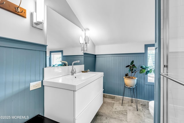 bathroom with lofted ceiling, vanity, wainscoting, toilet, and a shower with shower door