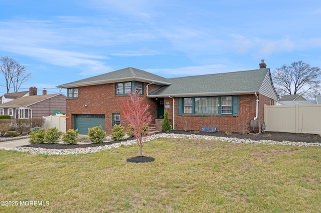 split level home with fence, an attached garage, a chimney, brick siding, and a front lawn