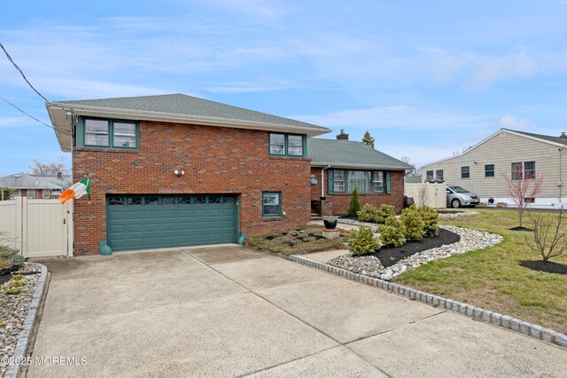 split level home featuring driveway, fence, an attached garage, brick siding, and a front lawn