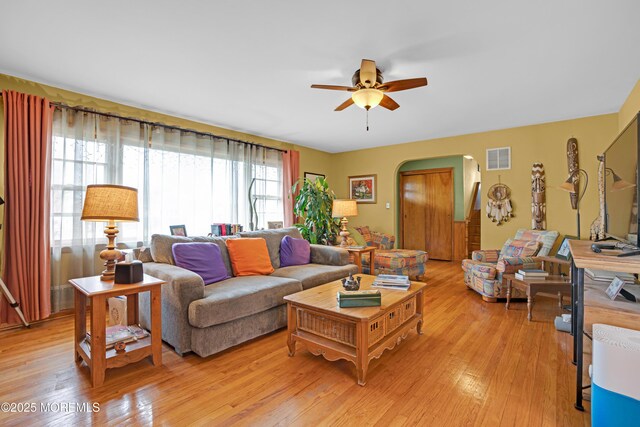 living room with arched walkways, visible vents, a ceiling fan, and light wood finished floors