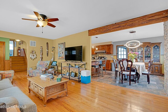 living area with visible vents, beamed ceiling, stairway, light wood-type flooring, and ceiling fan with notable chandelier