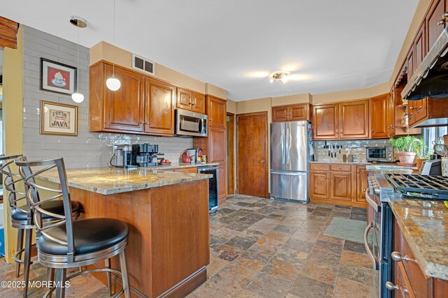 kitchen featuring visible vents, a peninsula, light stone countertops, stainless steel appliances, and ventilation hood