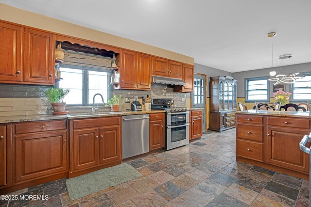 kitchen with a sink, stainless steel appliances, brown cabinetry, and under cabinet range hood