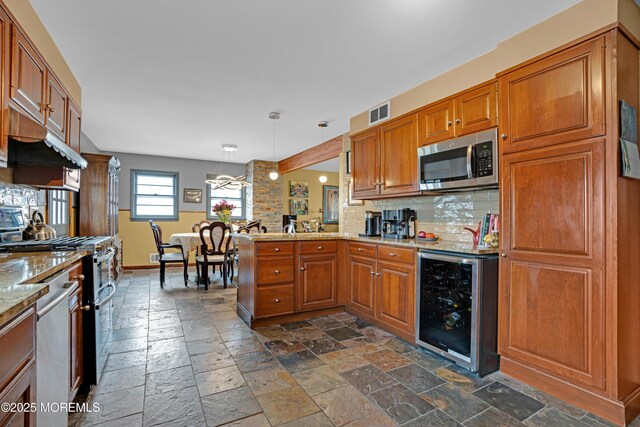 kitchen with stone tile flooring, wine cooler, appliances with stainless steel finishes, and brown cabinetry