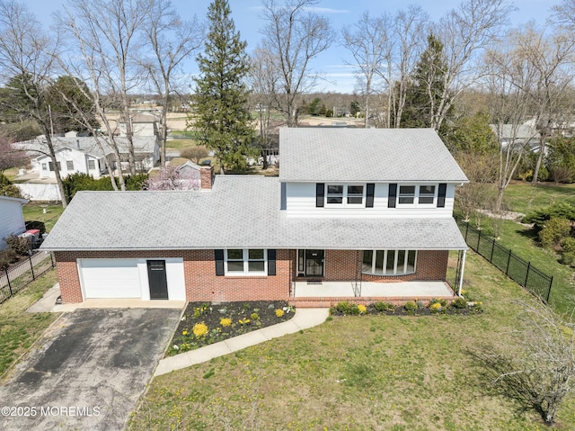 view of front facade with driveway, covered porch, fence, a front yard, and brick siding