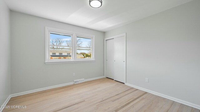 unfurnished bedroom featuring baseboards, wood finished floors, visible vents, and a closet