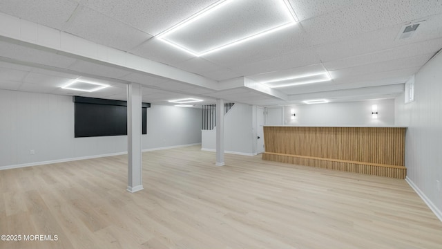 finished basement with a paneled ceiling, visible vents, baseboards, and wood finished floors
