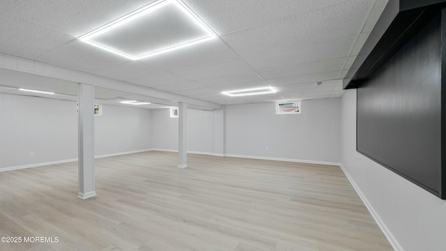 basement with light wood finished floors, baseboards, and a drop ceiling