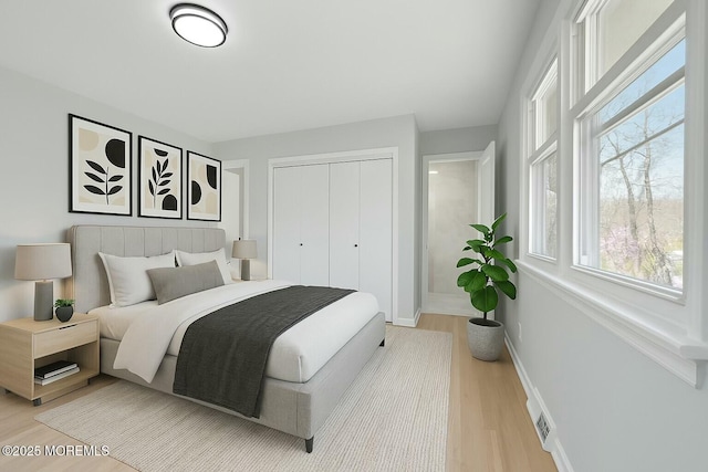 bedroom featuring light wood finished floors, baseboards, a closet, and multiple windows