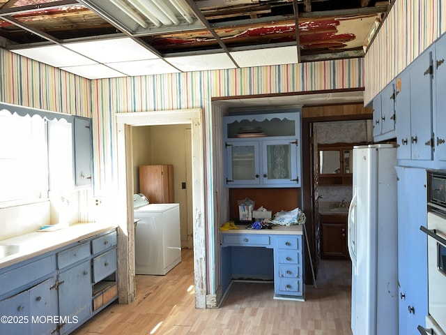 kitchen featuring light countertops, blue cabinets, wallpapered walls, freestanding refrigerator, and light wood-style flooring