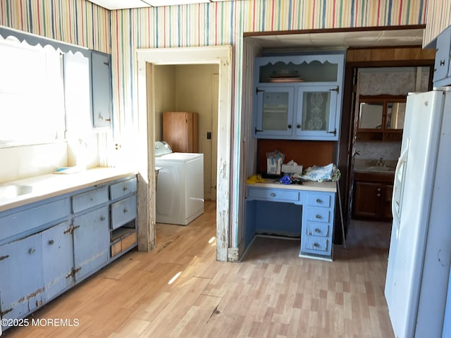 interior space with wallpapered walls, a sink, washer and dryer, and wood finished floors