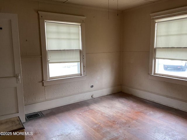spare room featuring wood finished floors, crown molding, a healthy amount of sunlight, and visible vents