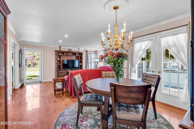 dining space with french doors, light wood-style floors, crown molding, and an inviting chandelier