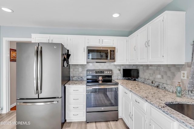 kitchen featuring decorative backsplash, light wood-type flooring, white cabinets, light stone counters, and stainless steel appliances