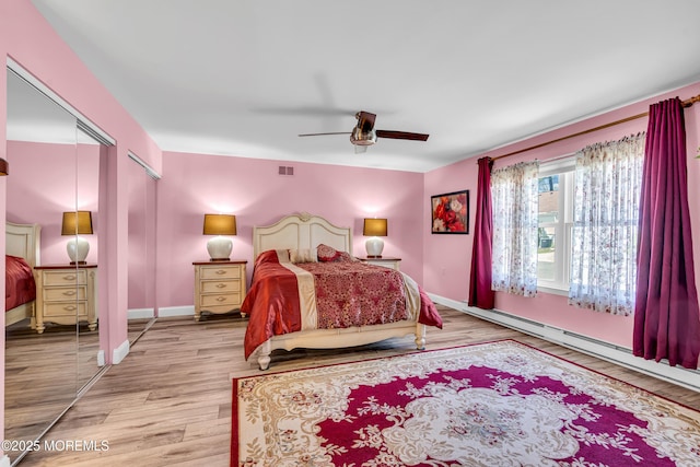bedroom with visible vents, a ceiling fan, wood finished floors, two closets, and a baseboard radiator