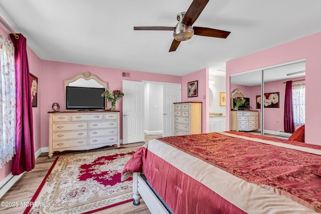 bedroom featuring a ceiling fan, visible vents, wood finished floors, baseboards, and ensuite bathroom