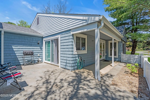 rear view of property with a shingled roof, a patio area, and fence