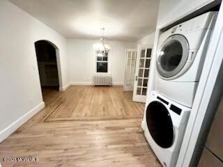 209 Broadway, Keyport, NJ 07735 - laundry area with radiator heating unit, stacked washing machine and dryer, baseboards, light wood-style flooring, and arched walkways