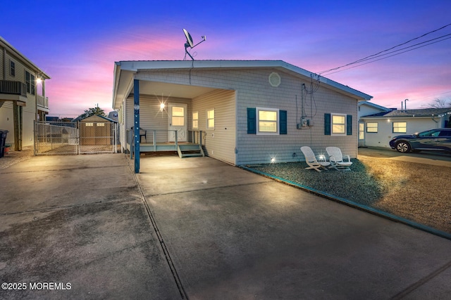back of house at dusk featuring driveway, a gate, an attached carport, and fence