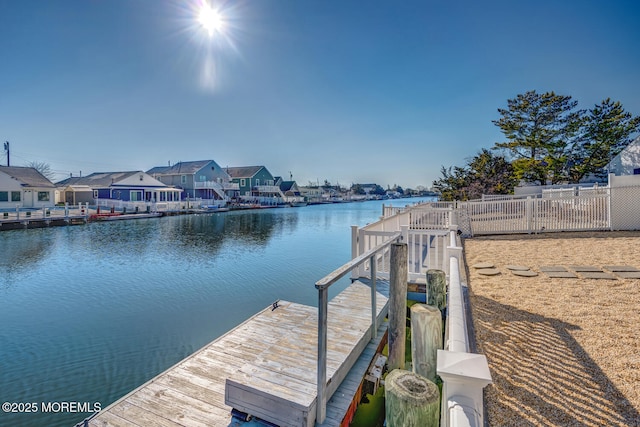 view of dock with a residential view, a water view, and fence