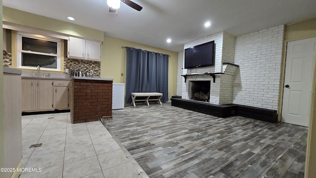 interior space with a brick fireplace, decorative backsplash, light wood finished floors, a sink, and ceiling fan