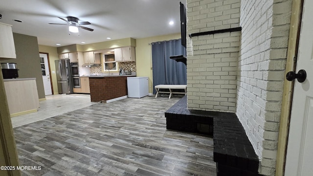 kitchen with wall chimney exhaust hood, appliances with stainless steel finishes, a ceiling fan, light wood finished floors, and backsplash